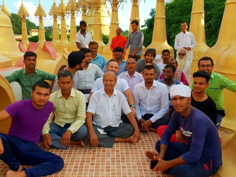 A group of men sitting in a serene and peaceful outdoor setting in Kanpur, India, at the conclusion of a 10-day silent meditation retreat. The men are seated in a circle on the ground and appear contemplative, reflecting the deep introspection and mindfulness cultivated during the retreat