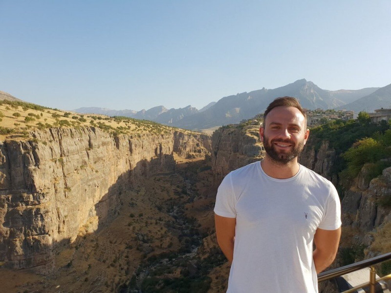 Mike Richards, author of 'Travelling Ape,' poses in front of the stunning Canyon in Rawanduz, located in northern Iraqi Kurdistan. The picturesque landscape features rugged cliffs and natural beauty, providing a breathtaking backdrop to Richards' exploration and storytelling.