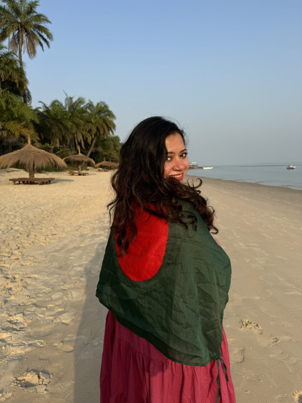 A picture of traveller Maliha Fairooz on the beach wrappen in a Bangladeshi flag