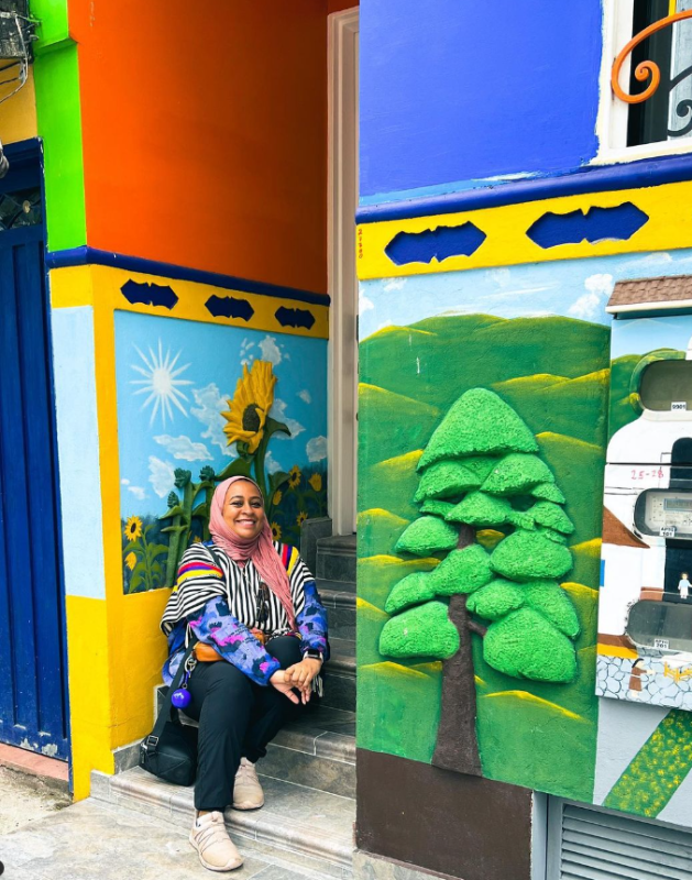 Rasha Yousif during her travels in South America, sitting in front of a colourful house in Colombia